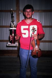 A man holding a fiddle and a trophy