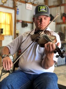 A man playing fiddle in a machine shed